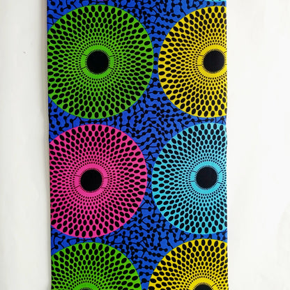 Fabric featuring a bold, colourful abstract pattern of concentric circular dots in pink, green, yellow, and blue on a dark blue background.