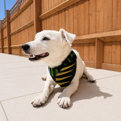 A white dog lying on a light tiled patio in front of a wooden fence, wearing a green and black striped pet bandana.
